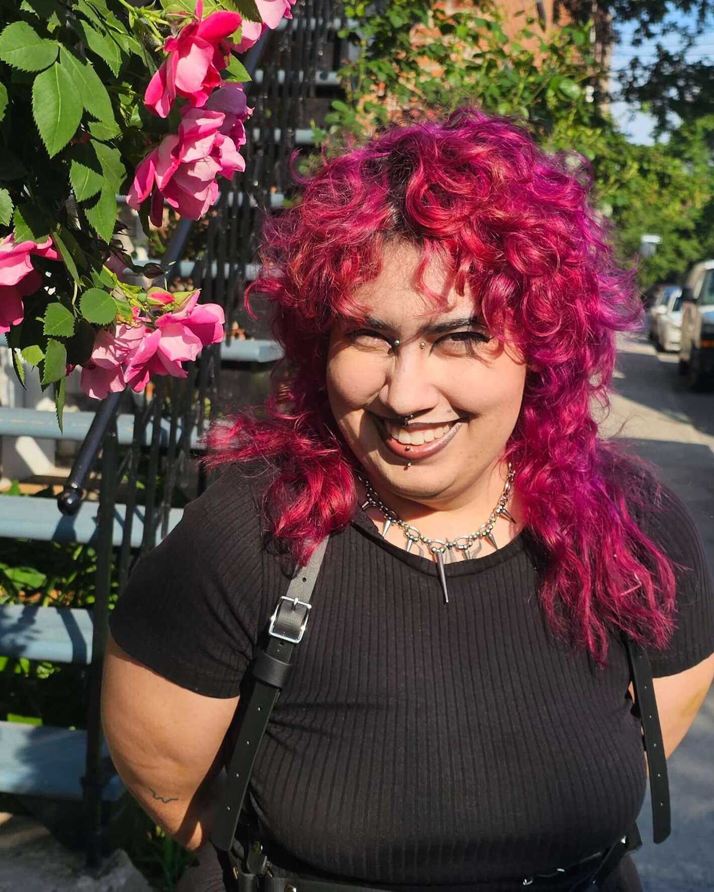 Magnus smiling on a sunlit sidewalk, beside climbing pink roses